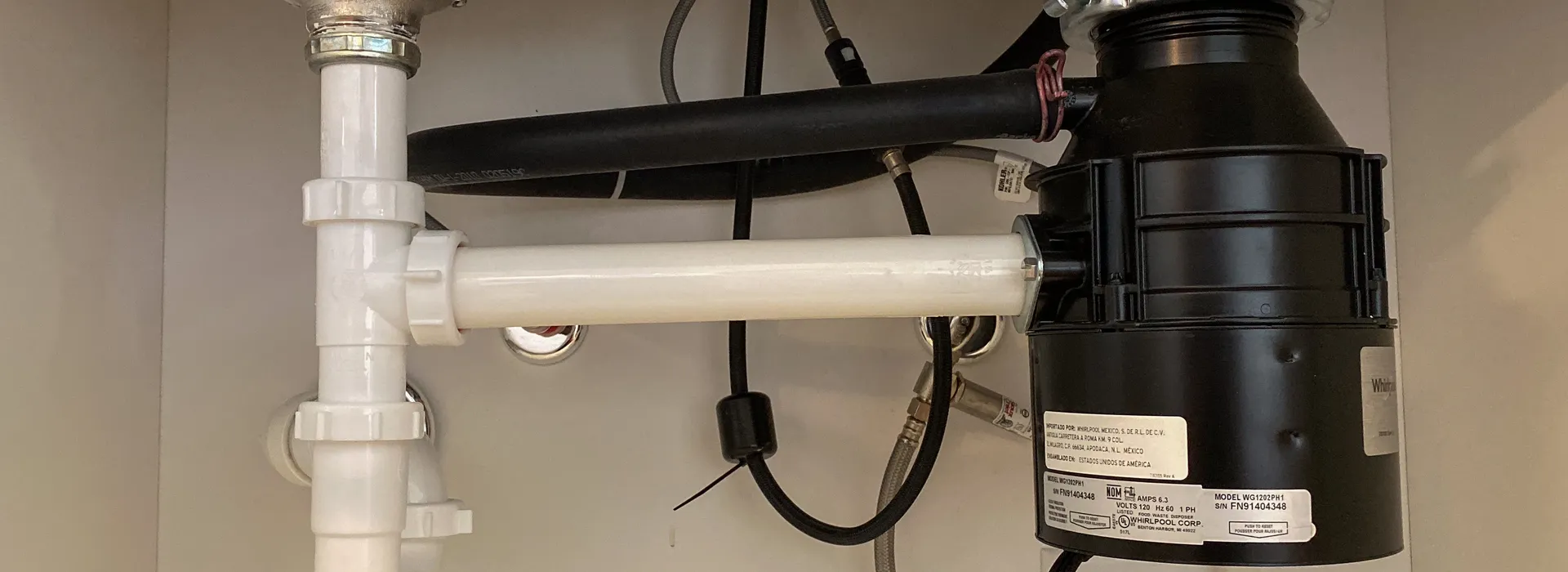 Garbage disposal installed under a double kitchen sink with new PVC drain lines and P-trap