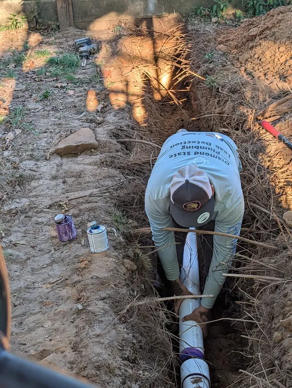 Technician fitting a new PVC sewer line through a root-filled trench